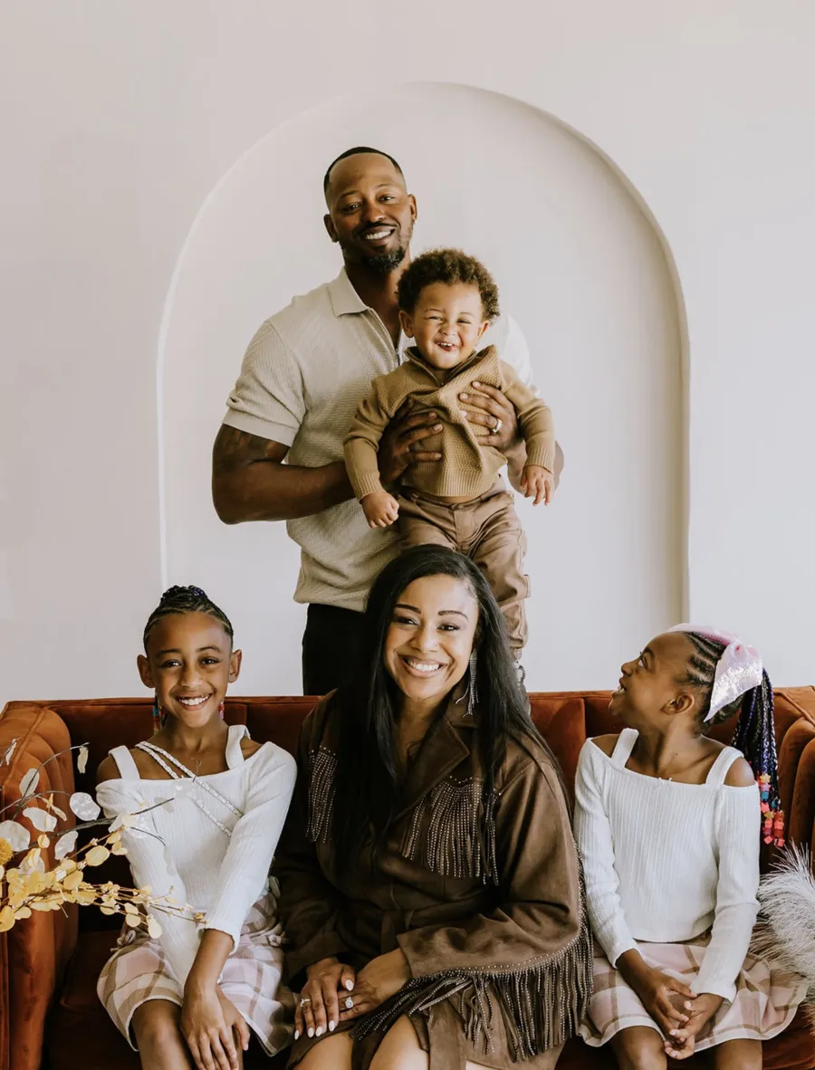 Meshayla Kemp with her husband and their three children, smiling on a rust-colored sofa